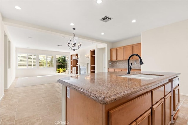 kitchen featuring sink, light stone counters, an island with sink, pendant lighting, and decorative backsplash