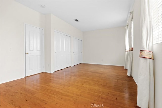 unfurnished bedroom with hardwood / wood-style floors and multiple closets