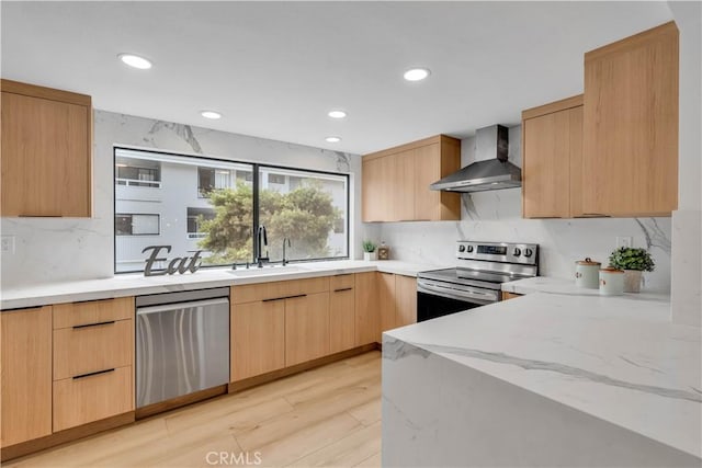 kitchen featuring wall chimney exhaust hood, light brown cabinets, stainless steel appliances, sink, and light wood-type flooring