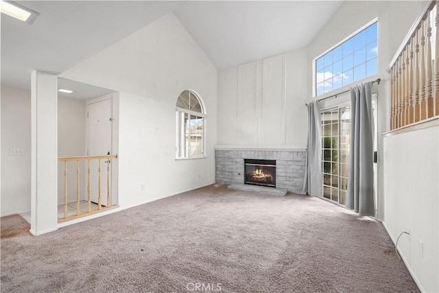 unfurnished living room with high vaulted ceiling, carpet floors, a brick fireplace, and a healthy amount of sunlight