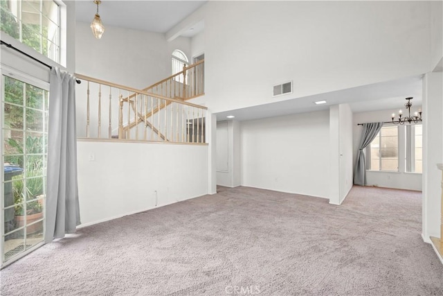 unfurnished living room featuring carpet, a healthy amount of sunlight, a high ceiling, and a notable chandelier