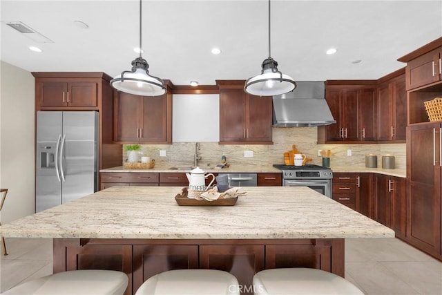 kitchen with wall chimney range hood, sink, hanging light fixtures, a kitchen bar, and stainless steel appliances