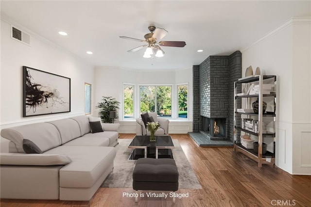 living room featuring hardwood / wood-style floors, ornamental molding, a brick fireplace, and ceiling fan