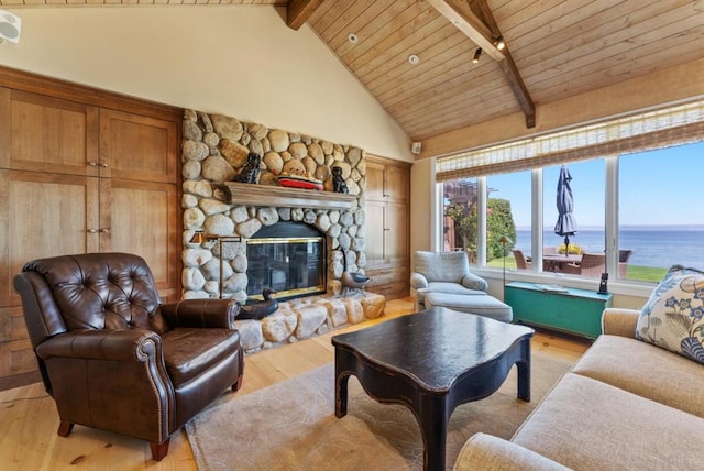 living room with high vaulted ceiling, a water view, light hardwood / wood-style floors, a stone fireplace, and beamed ceiling