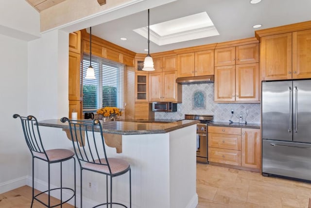 kitchen featuring decorative light fixtures, premium appliances, kitchen peninsula, dark stone counters, and backsplash