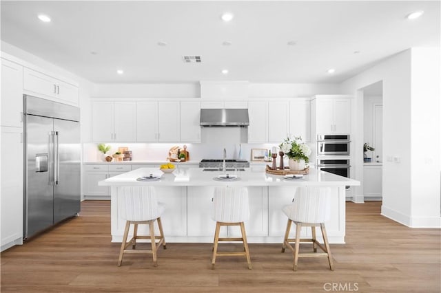 kitchen with a kitchen island with sink, appliances with stainless steel finishes, white cabinetry, and a kitchen bar