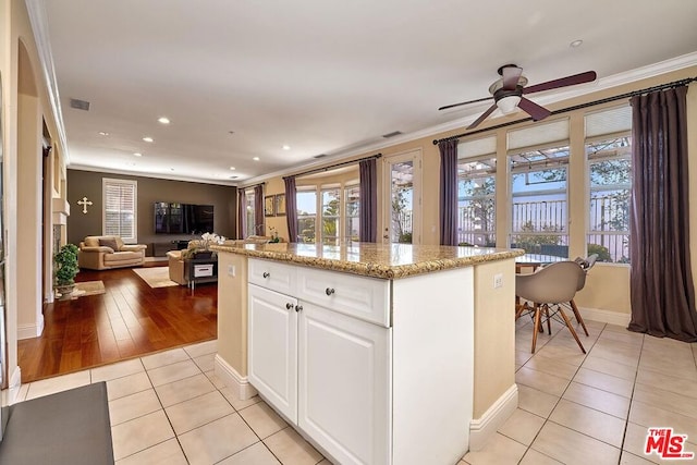 kitchen with ceiling fan, a center island, light tile patterned flooring, white cabinetry, and ornamental molding