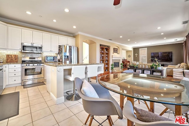 kitchen featuring light tile patterned floors, white cabinetry, stainless steel appliances, light stone counters, and a center island