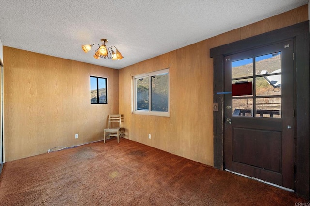 carpeted foyer featuring wood walls, a textured ceiling, and a notable chandelier