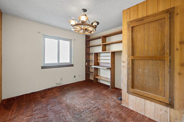 unfurnished bedroom with a textured ceiling, a chandelier, and dark colored carpet