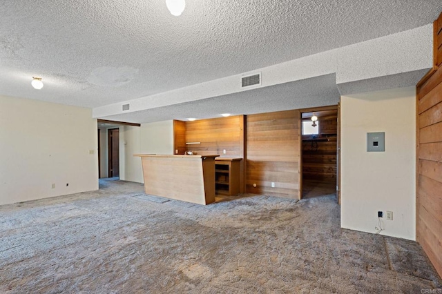 unfurnished living room with wooden walls, a textured ceiling, and carpet flooring