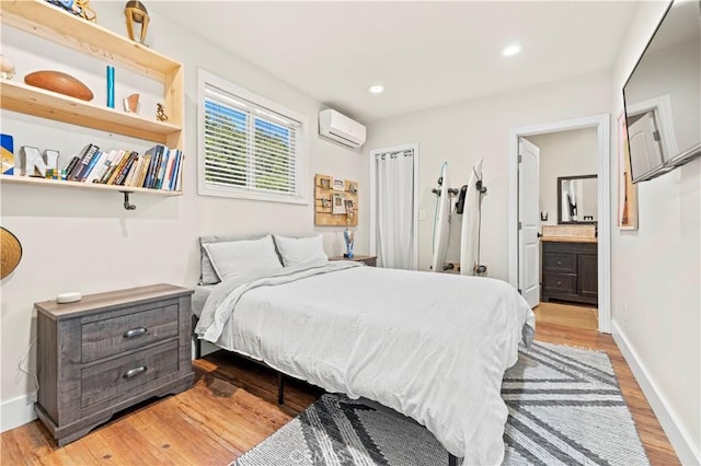 bedroom with a wall mounted AC, connected bathroom, and light hardwood / wood-style floors