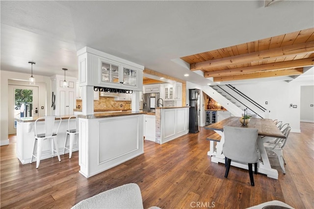 interior space with decorative light fixtures, kitchen peninsula, beamed ceiling, white cabinets, and wooden ceiling