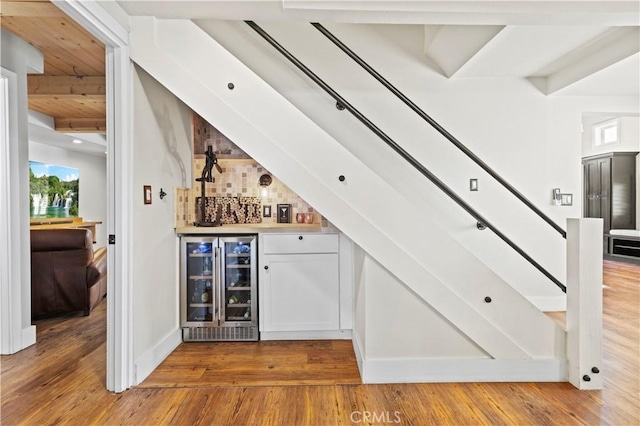 bar featuring white cabinets, wood-type flooring, beverage cooler, and beam ceiling