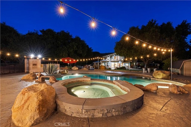 pool at twilight with an in ground hot tub and a patio area