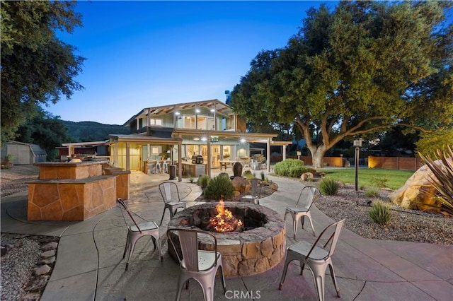 patio terrace at dusk with a mountain view, an outdoor fire pit, and a balcony