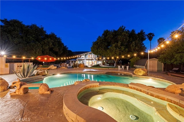 pool at twilight with a storage unit and an in ground hot tub