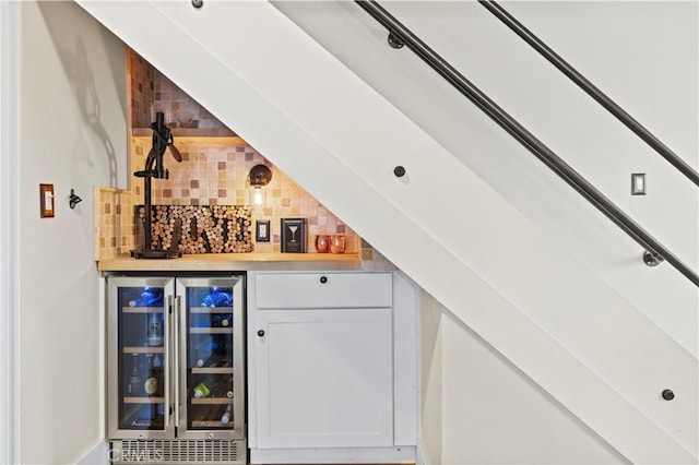 bar with wine cooler, backsplash, and white cabinetry