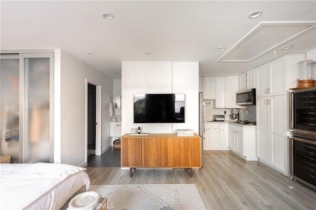 kitchen featuring white cabinets, light wood-type flooring, beverage cooler, and stainless steel appliances