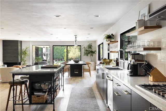 kitchen with decorative light fixtures, a kitchen bar, light hardwood / wood-style floors, sink, and stainless steel gas cooktop