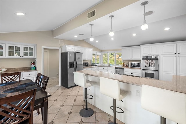 kitchen with white cabinets, vaulted ceiling, appliances with stainless steel finishes, and pendant lighting