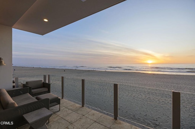 balcony at dusk featuring a water view, an outdoor hangout area, and a view of the beach