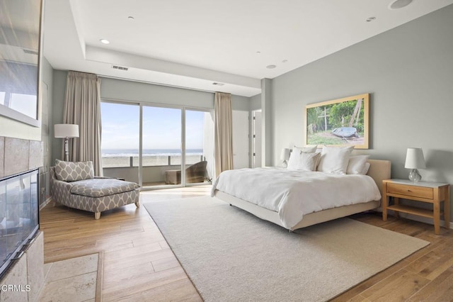 bedroom featuring a tiled fireplace, access to exterior, a water view, and light hardwood / wood-style floors
