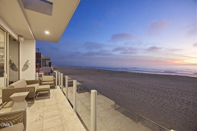 balcony at dusk featuring a beach view, outdoor lounge area, and a water view