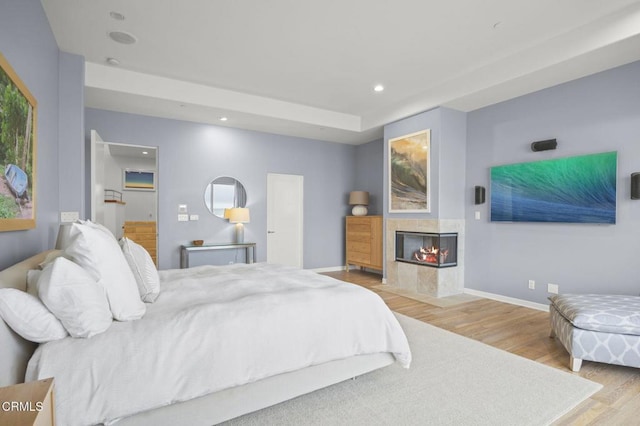 bedroom with a tile fireplace and light hardwood / wood-style flooring