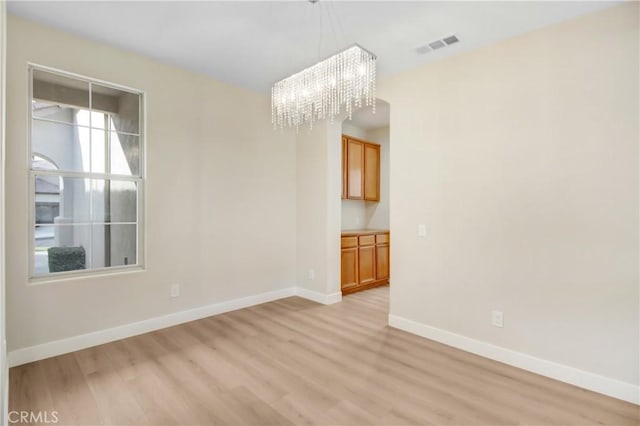 spare room featuring light wood-type flooring and a notable chandelier