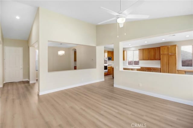 unfurnished living room with high vaulted ceiling, light wood-type flooring, and ceiling fan with notable chandelier