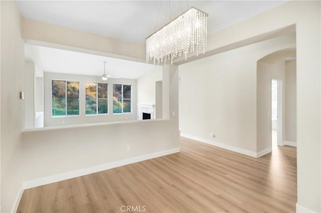 unfurnished living room with ceiling fan with notable chandelier, light hardwood / wood-style flooring, and vaulted ceiling