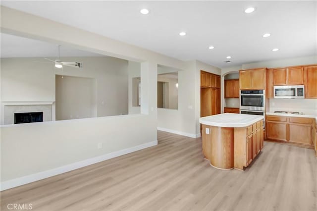 kitchen featuring a center island, double oven, light hardwood / wood-style floors, ceiling fan, and white gas cooktop