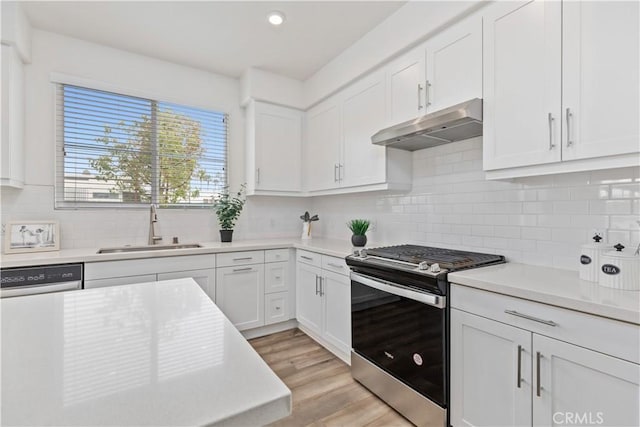 kitchen with appliances with stainless steel finishes, white cabinetry, decorative backsplash, sink, and light wood-type flooring