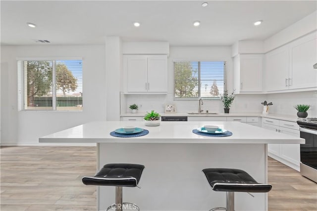 kitchen with white cabinetry, a center island, electric stove, a kitchen breakfast bar, and sink