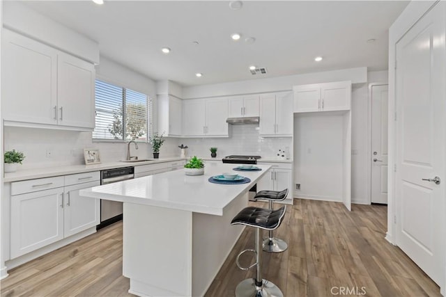 kitchen with white cabinets, a center island, appliances with stainless steel finishes, a kitchen bar, and sink