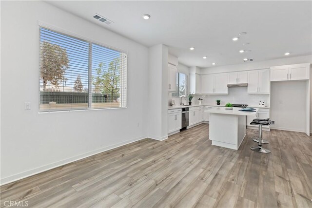 kitchen featuring stainless steel dishwasher, a breakfast bar area, white cabinetry, and a kitchen island