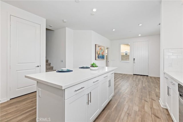 kitchen with white cabinetry, light hardwood / wood-style flooring, tasteful backsplash, and a kitchen island