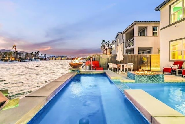 pool at dusk featuring pool water feature and a water view