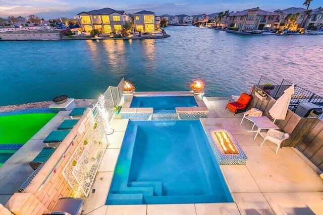 pool at dusk with a water view, pool water feature, and a patio