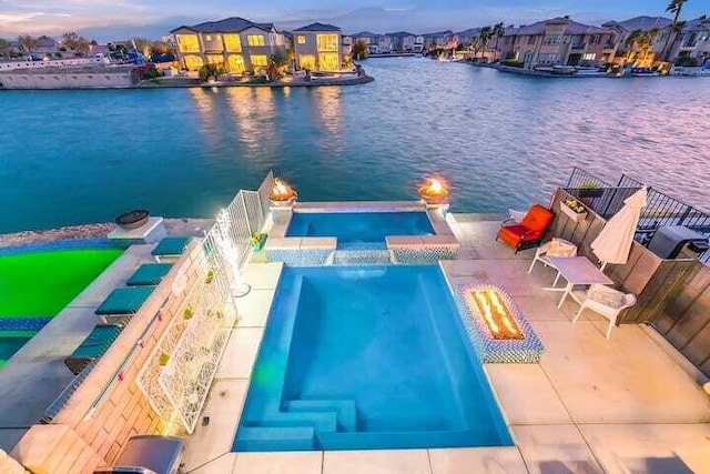 pool at dusk with pool water feature, a water view, and a patio