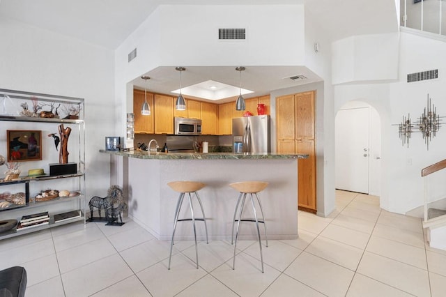 kitchen featuring light tile patterned floors, kitchen peninsula, stainless steel appliances, decorative light fixtures, and dark stone counters