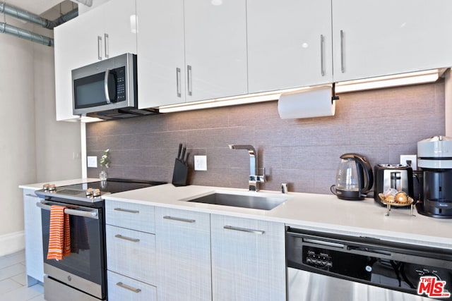 kitchen with white cabinets, appliances with stainless steel finishes, tasteful backsplash, sink, and light tile patterned floors