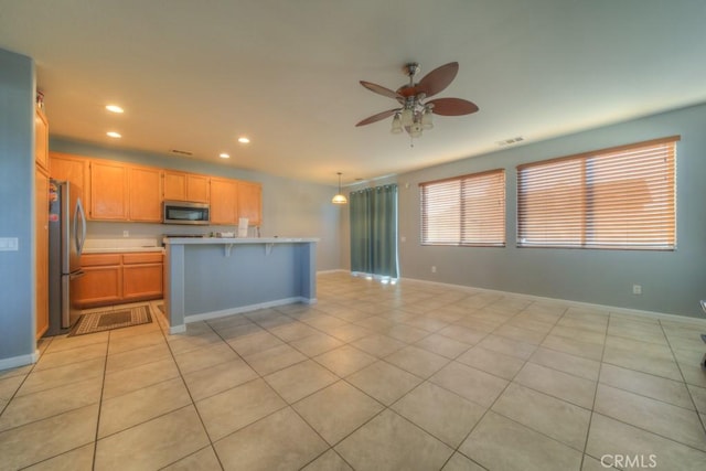 kitchen featuring ceiling fan, appliances with stainless steel finishes, a kitchen bar, and light tile patterned flooring