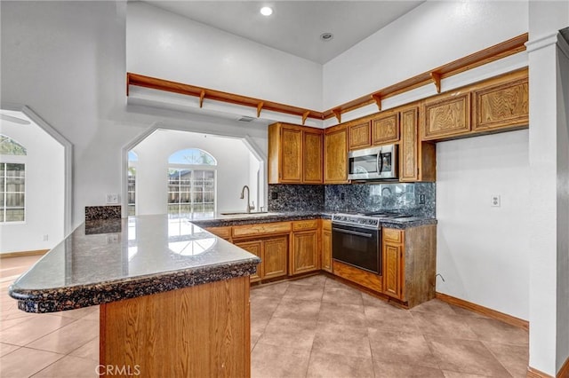 kitchen featuring appliances with stainless steel finishes, a towering ceiling, tasteful backsplash, sink, and kitchen peninsula