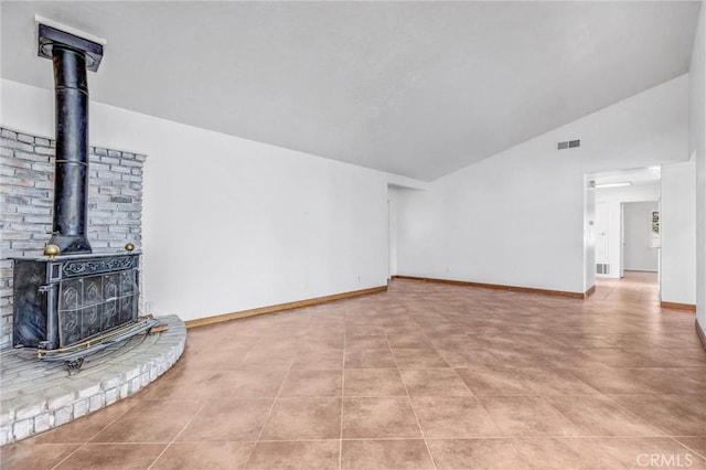 unfurnished living room with light tile patterned floors, vaulted ceiling, and a wood stove