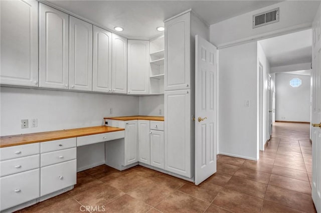 kitchen featuring wood counters, built in desk, and white cabinets