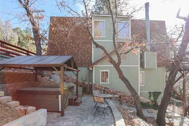 rear view of house featuring a patio area, a hot tub, a shingled roof, and a gazebo