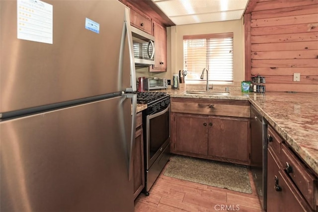 kitchen with light stone counters, sink, stainless steel appliances, and light wood-type flooring