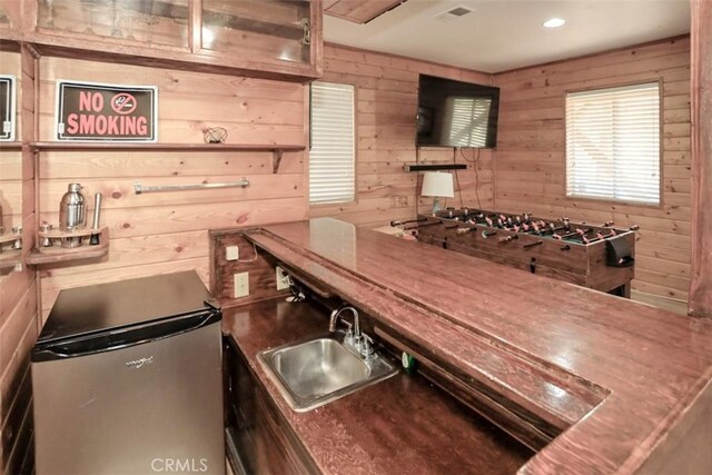 kitchen featuring sink, stainless steel refrigerator, and wooden walls